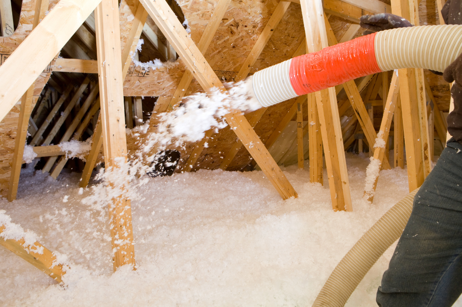 A professional using roofing insulation equipment to blow loose-fill cellulose insulation in an attic.