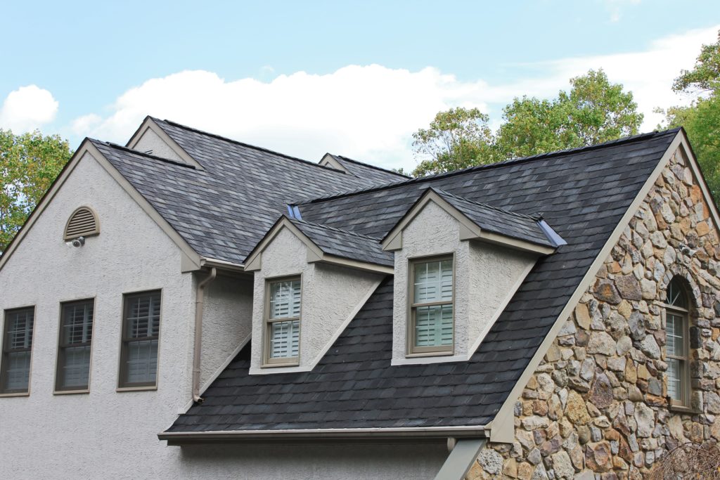 A beige and stone house with a dark grey shingle roof.